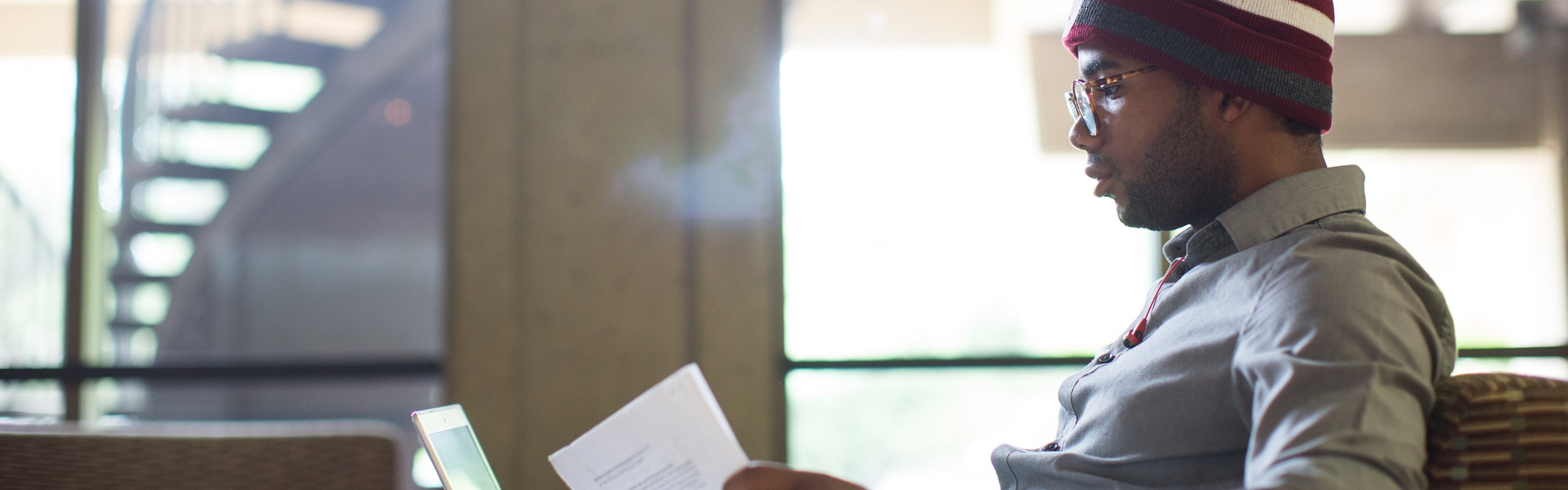 Profile of a student with a paper in his hand and looking at his laptop