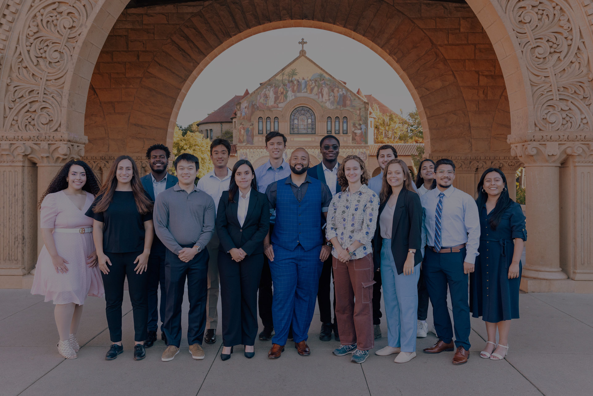 Members of the 2023 Summer First cohort pose for picture in front of an archway at the Stanford campus main quad.