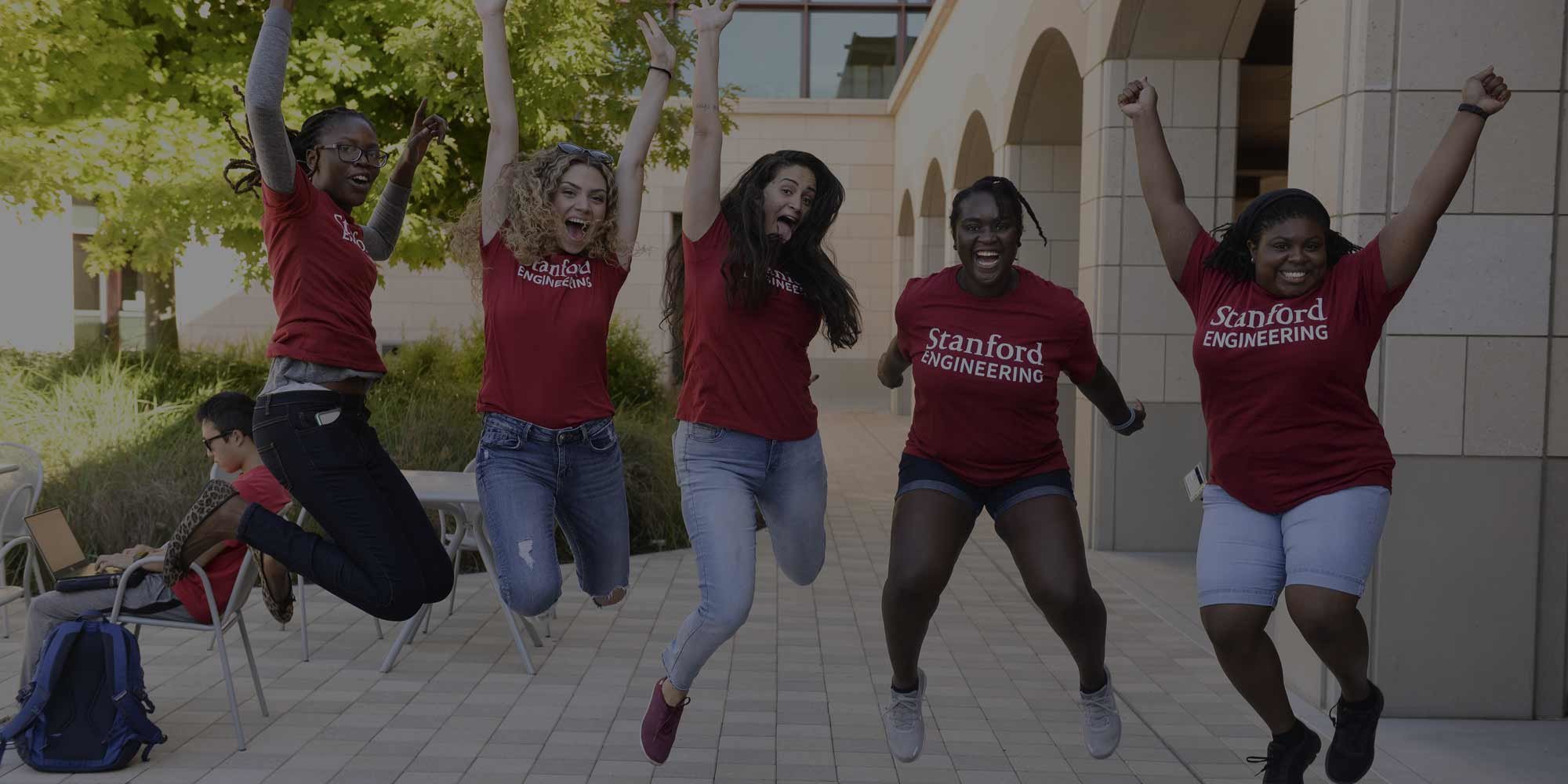 Five students mid-air after they jump for the camera. They're wearing their newly-acquired, Stanford Engineering t-shirts