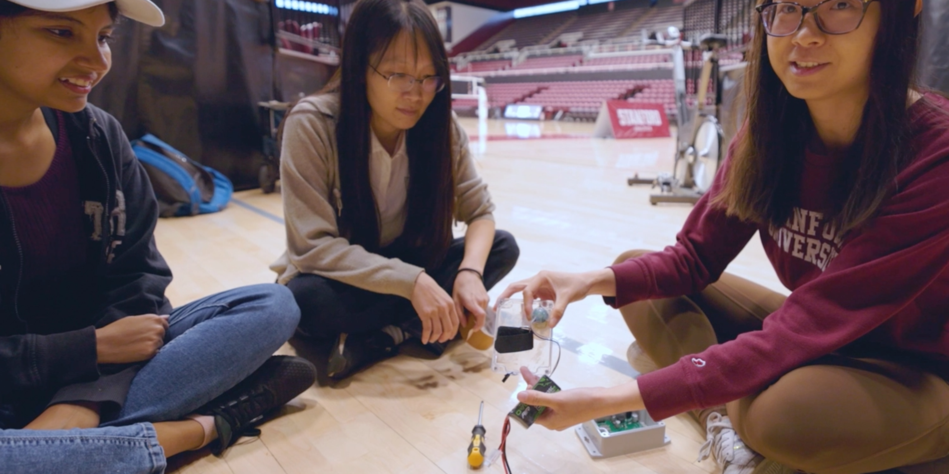 Professor and two students assembling sensors while sitting on the floor of a gymnasium.
