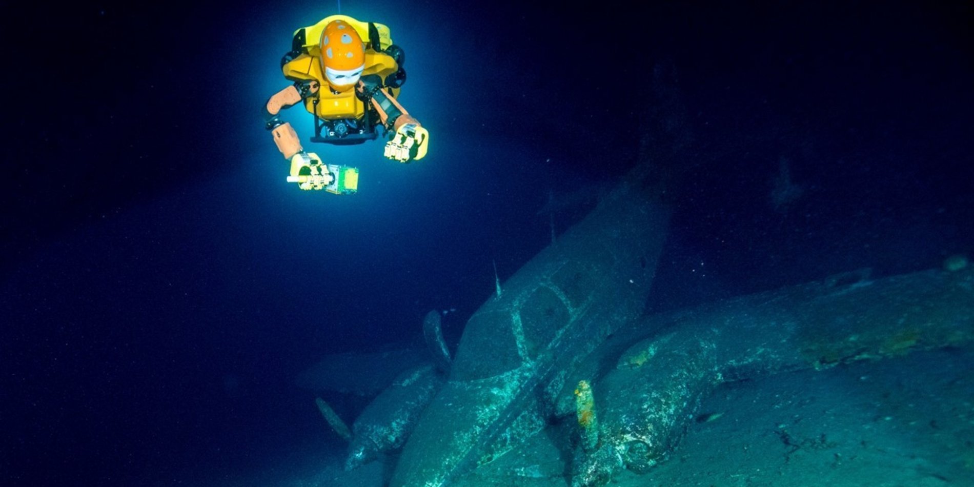 A robotic diver swims above a sunken plane underwater.