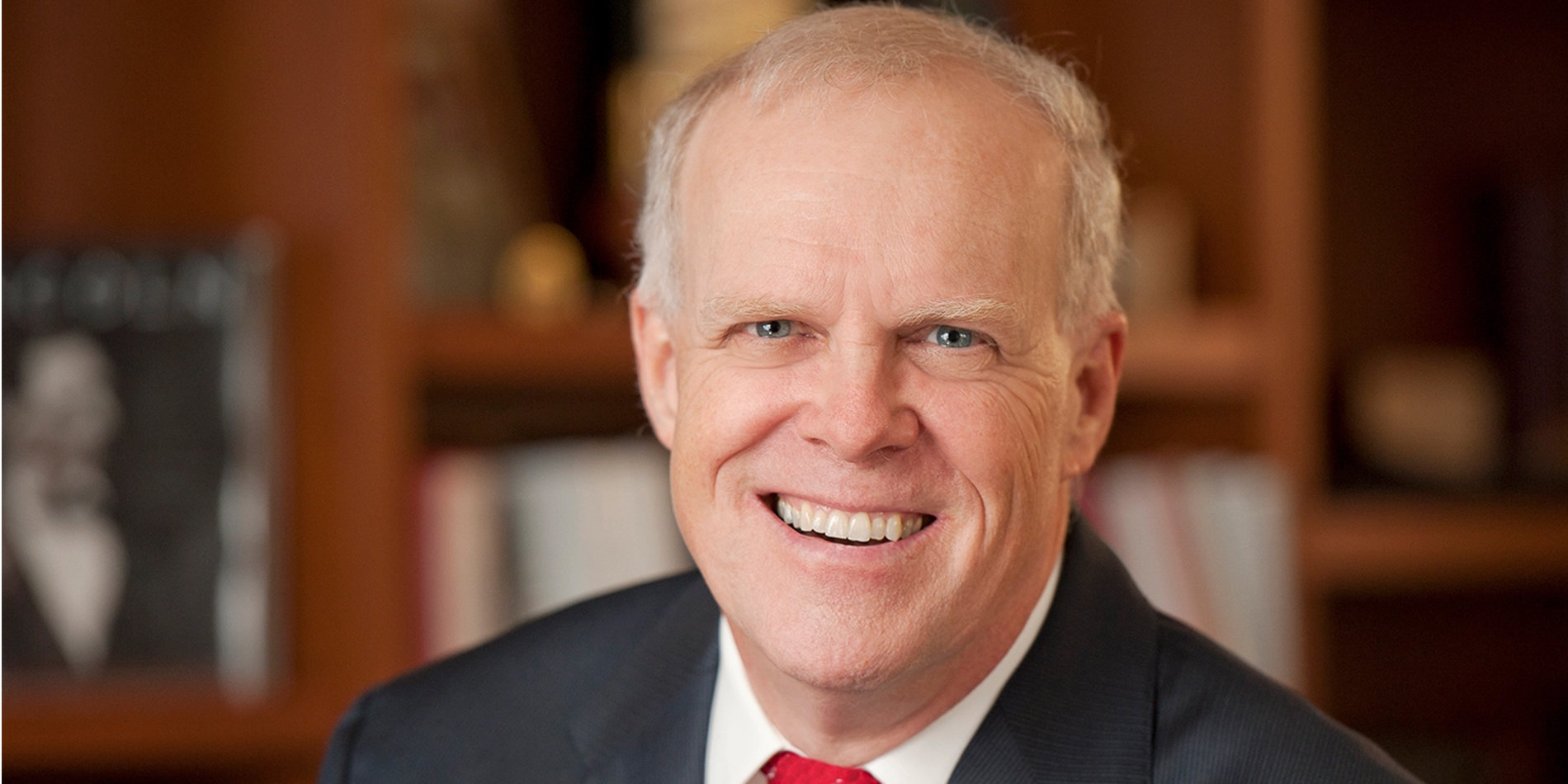 Portrait of John Hennessy wearing a black suit and red tie. 
