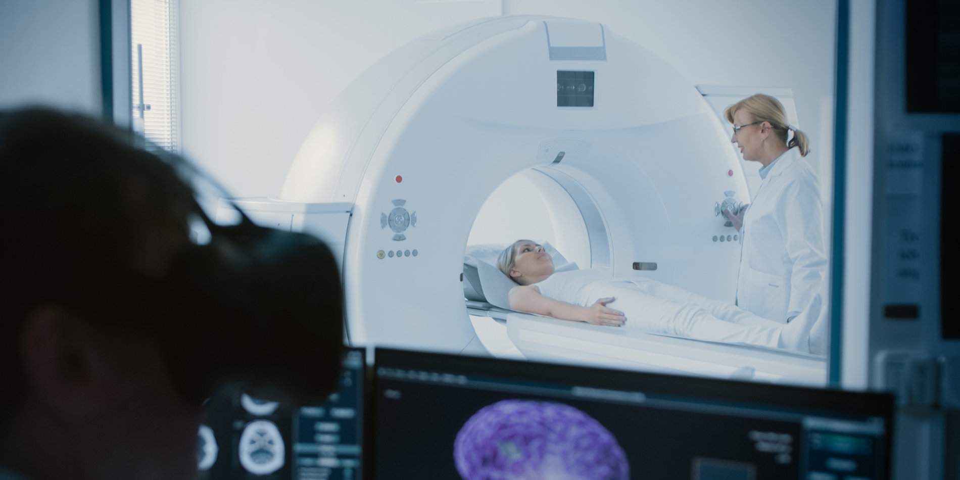 Photo of a patient undergoing a CT scan, while a doctor wears a virtual reality headset.