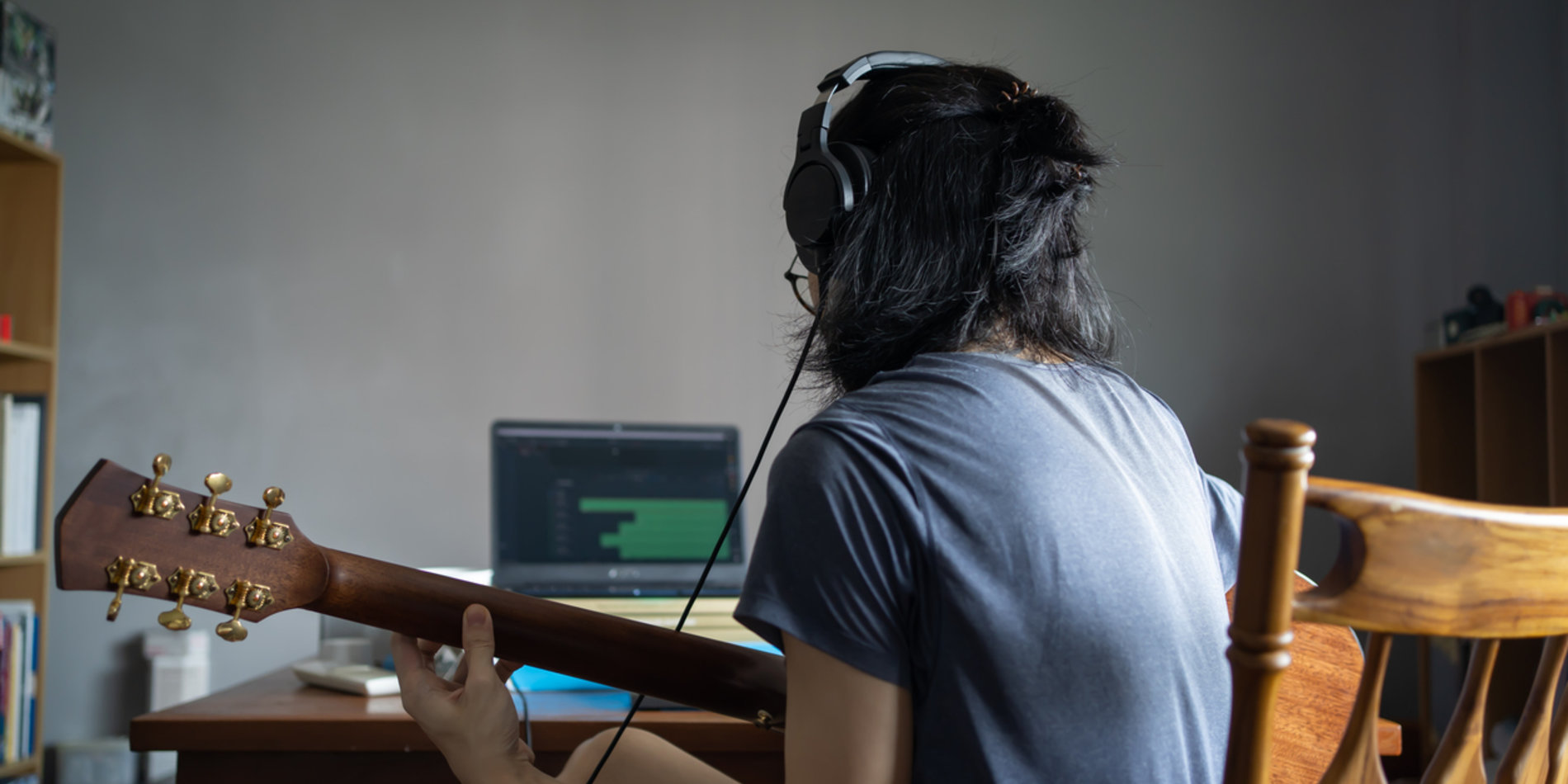  A person with headphones using a digital audio workstation on a computer while holding a guitar.