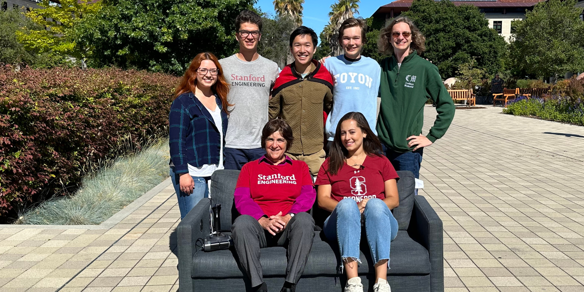 A group photo of Stanford students and the Stanford Engineering Dean sitting on and standing near a motorized couch.