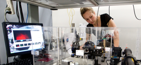 Student in lab looking into machine with computer monitor next to her