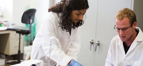 One student looking over another's paper with both in lab coats